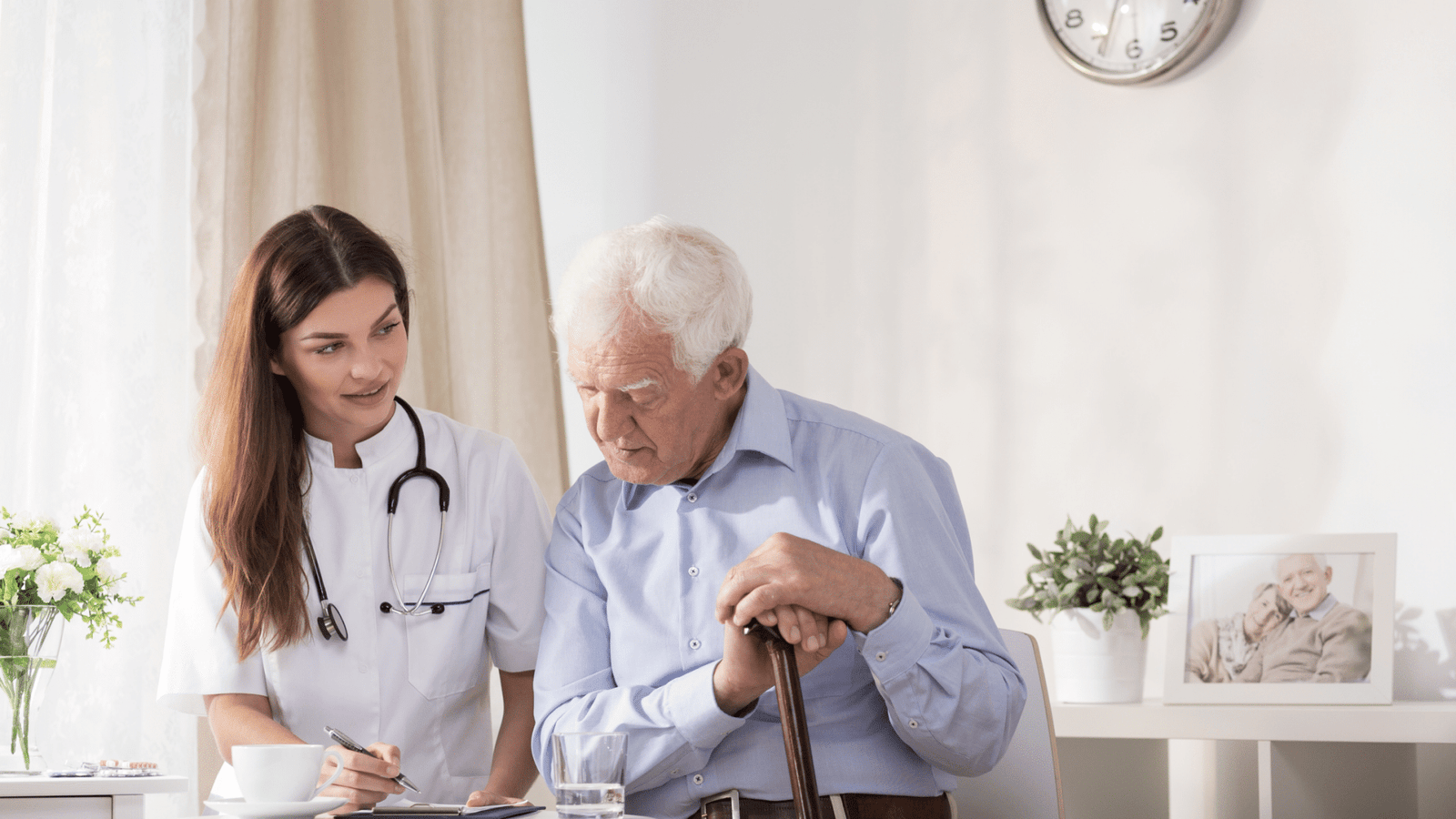 Skilled Services - An elderly man holding a cane sitting next to a nurse, looking down at what she's writing on her clipboard.
