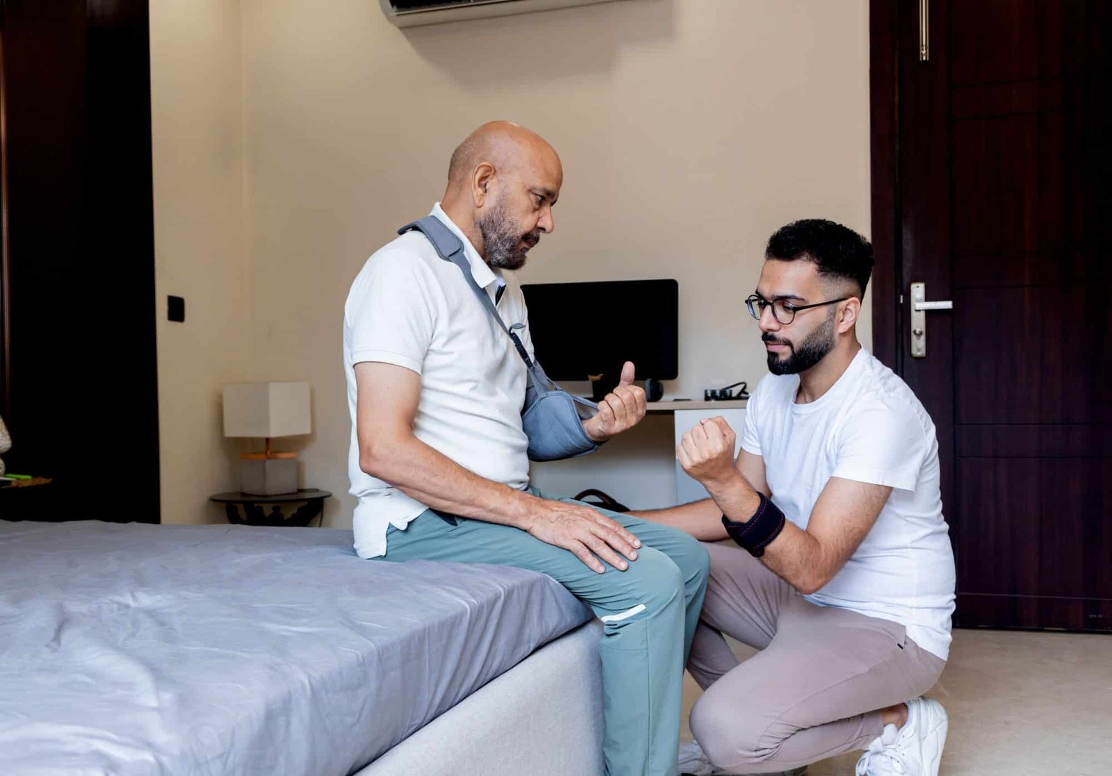 Post-Surgery Care - Nurse with man whose arm is in a sling, sitting on a bed